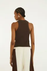 Musculosa de algodón elastizado color marrón, con cuello redondo y sisas amplias. Presenta un bordado frontal con la palabra "Rio" en tonos blancos y celestes.