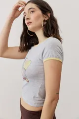Remera corta gris melange con ribetes amarillos en el cuello y las mangas, y un estampado gráfico abstracto en el pecho.