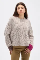 Sweater de tejido de punto con diseño jaspeado en tonos beige y marrón, de corte holgado y cuello redondo. Presenta mangas largas con puños en colores contrastantes, uno en marrón oscuro y otro en fucsia.