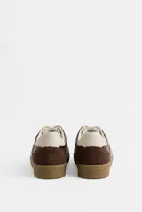 Zapatilla urbana color chocolate, confeccionada en una combinación de cuero y gamuza, con cordones y suela de goma.