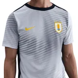 Camiseta de fútbol Nike de la selección uruguaya, modelo alternativo o de entrenamiento, color blanco con un patrón gráfico sutil de líneas diagonales grises. Presenta cuello redondo negro y logo Nike y escudo de la AUF en dorado.