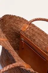 Bolso tipo tote de cuero vacuno, completamente trenzado a mano. El color es marrón oscuro, casi chocolate. Posee dos asas de hombro trenzadas.