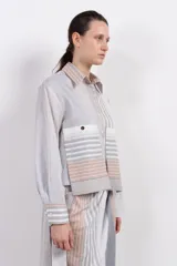 Camisa corta de algodón y seda con silueta recta, diseño a rayas verticales en tonos gris, blanco y beige, cuello camisero, cierre frontal con botones, mangas largas con puños abotonados, bolsillos de parche con botón a presión en el pecho y bajo recto.