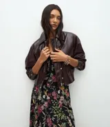 Campera bomber de cuero sintético color marrón oscuro, con cuello camisero, cierre frontal con botones metálicos y elástico en el ruedo.