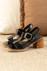 Sandalias de cuero charol negro con diseño de tiras, cierre de hebilla metálica dorada y taco cuadrado de madera.