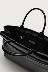 Bolso de mano extragrande negro de cuero sintético, con compartimento principal con cierre de imán, bolsillo interior con cierre y bolsillo secundario con solapa y detalle de cinta. Cuenta con dos asas de mano.