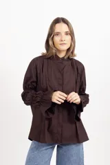 Camisa blanca de corte recto con cuello mao y cierre frontal oculto. Destaca por sus mangas largas con múltiples frunces que generan volumen y terminan en puños acampanados.