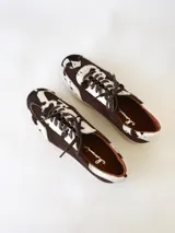 Zapatilla deportiva de cuero con estampado de vaca (pelo), color marrón y blanco. Suela blanca gruesa.