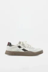 Zapatillas urbanas de cuero en tono off-white, con detalles en color marrón oscuro y suela de goma texturizada en contraste. Presentan cordones al tono y logo de la marca grabado en el lateral.