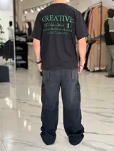 Remera oversize color beige, con diseño estampado en la espalda que incluye tipografía grande y texto descriptivo en negro.