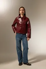 Chaqueta de eco-cuero negro con acabado brillante, cuello camisero, cierre frontal con botones y mangas largas.