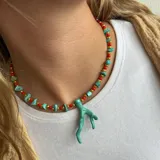Collar corto con cuentas pequeñas rojas y doradas, intercaladas con piedras irregulares color turquesa. Dije central en forma de coral color turquesa.