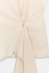 Camisa color crema de la colección Zara Woman, confeccionada en algodón 100%. Presenta cuello subido, manga sisa y un detalle de tejido tipo fajín asimétrico con un nudo en el lateral. El cierre frontal es con botones ocultos.