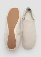 Zapatos tipo ballerinas planas de piel ovina en color blanco, con punta redonda, diseño sin cordones y detalle de fruncido elástico en el talón.