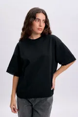 Remera negra de manga corta con detalles de encaje en el ruedo y las terminaciones de las mangas, de corte holgado y cuello redondo.