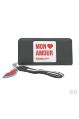 Billetera tipo clutch color negro con textura de cuero sintético. Presenta un parche frontal blanco con el texto "MON AMOUR" en rojo y el logo "Oreiro Love". Incluye un llavero desmontable con forma de labios rojos y azules, y una correa de muñeca negra con rayas blancas.