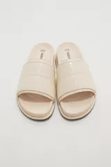 Sandalias planas color marfil, con tira ancha acolchada en el empeine y suela baja con borde oscuro.