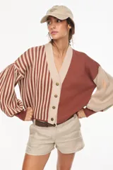 Cardigan tejido bicolor con diseño asimétrico que combina rayas verticales en un lado y un tono liso en el otro, de ajuste relajado, cuello en V y mangas abullonadas.