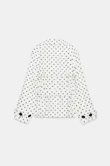 Cazadora estilo trench corta confeccionada en lino, con diseño de lunares negros sobre fondo blanco. Cuenta con cuello solapa, manga larga con trabillas en los puños, cierre frontal cruzado con botones negros y cinturón ajustable del mismo tejido.