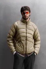 Campera puffer color beige con cuello alto, cierre frontal con cremallera y bolsillos laterales con cierre. Diseño acolchado horizontal.