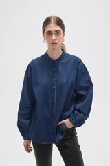 Camisa de jean azul con cuello mao, cierre frontal con botones y mangas largas con puños elásticos fruncidos.
