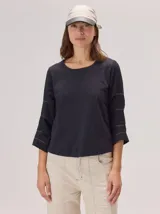 Remera de algodón color blanco, con cuello redondo y mangas tres cuartos con volados escalonados y detalles de pespuntes.