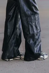 Pantalón cargo de ecocuero negro, de corte holgado y tiro medio-alto. Presenta bolsillos laterales tipo cargo y costuras visibles a lo largo de las piernas.