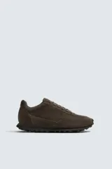 Zapatilla deportiva de hombre confeccionada en piel con acabado de serraje. Presenta un diseño de paneles combinados, cierre con cordones y suela dentada de goma.