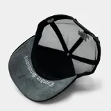 Gorra tipo trucker color negro con panel frontal bordado que presenta el logo 'LA' y diseño de llamas tribales en tonos gris y blanco. Cuenta con parte trasera de malla ajustable.