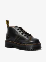 Botas Dr. Martens modelo Church Quad de cuero negro, con plataforma gruesa acanalada, costuras amarillas contrastantes y cordones negros.