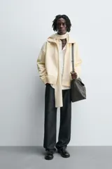 Sudadera color crema de algodón con interior afelpado, corte relajado, cuello subido y manga larga. Presenta bolsillos de vivo en la cadera y acabados en rib, con cierre frontal de cremallera.