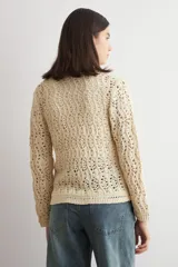 Cardigan de punto calado color beige, con cuello redondo y cierre frontal de botones.