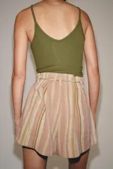Bermuda de tiro medio con diseño de rayas verticales en tonos rosados y beige. Presenta cintura con trabillas, cinturón ajustable con lazada, bolsillos laterales y detalle de pliegues en el delantero.