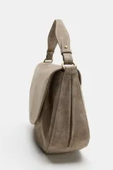 Bolso bandolera de piel gamuzada color gris topo, con solapa curva, asa de mano corta y herrajes metálicos dorados.