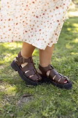 Sandalias de cuero marrón con diseño de tiras entrecruzadas y hebilla lateral. Plataforma track color negro.