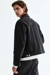 Campera trucker de denim rígido en color negro, con cuello camisero, cierre frontal de botones metálicos, bolsillos con solapa en el pecho y bolsillos laterales.