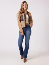 Chaqueta de corte boxy confeccionada en tejido de punto color crema, con detalles en cuero sintético negro en cuello, solapas, cartera central y bolsillos frontales. Presenta cierre frontal con botones metálicos plateados y costuras decorativas visibles.