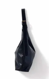 Cartera negra de cuero sintético con textura granulada, forma trapezoidal y asa de hombro ajustable con hebilla metálica.