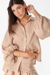 Camisa de lino color beige, de corte holgado y mangas abullonadas con volumen. Presenta cuello camisero y cierre frontal con botones.