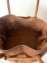 Bolso grande de cuero marrón con textura tipo cocodrilo, estructura rígida y asas para llevar al hombro. Tiene una tira con tachas y hebillas en cada extremo, también lleva lazos en los costados.