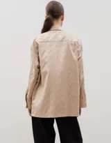 Camisa de corte holgado y diseño clásico, confeccionada en tela satinada con un sutil estampado floral tono sobre tono. Presenta cuello camisero, cierre frontal con botones y mangas largas con puños rectos.