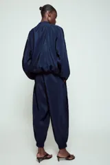 Pantalón de tiro alto de tela satinada color azul marino, con bolsillos frontales, cintura ajustable con cordones y puños elásticos en los tobillos.