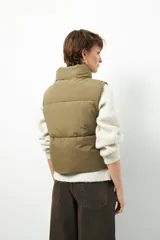 Chaleco puffer color beige, sin mangas, con cuello alto y cierre frontal con cremallera.