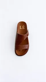 Sandalias de cuero color marrón con diseño asimétrico de tiras y plantilla anatómica. Tienen ajuste lateral con velcro y suela plana.