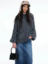 Sweater de tejido de punto color marrón con textura tipo waffle, diseño amplio, hombros caídos y cuello redondo. Presenta un bolsillo frontal aplicado y mangas con puños anchos decorados con botones.