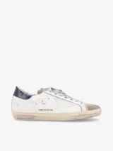 Zapatillas urbanas Golden Goose modelo Super-Star, de cuero blanco con efecto desgastado, estrella lateral en cuero perforado, puntera en gamuza gris, talón en cuero azul marino y cordones grises.
