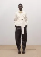 Chaqueta de mezcla de lana, poliéster y elastano color marfil, con solapas cruzadas, cuello alto y cinturón ajustable del mismo tejido. Cuenta con mangas largas y forro interior de viscosa.