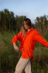 Camisa de calce relajado y corte recto color naranja, con cuello clásico, mangas largas con puños abotonados y cierre frontal con botones.