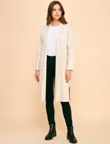 Cardigan largo de tejido color beige claro, sin cuello, con bolsillos frontales y detalles de pespuntes decorativos a lo largo del borde frontal.