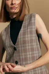 Chaleco sastrero de corte entallado con estampado de cuadros en tonos beige, marrón y azul. Presenta escote en V, cierre frontal con botones y terminación en punta en el ruedo. Incluye ajuste con hebilla en la espalda.